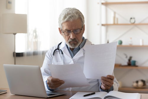 A doctor reading papers in front of a laptop